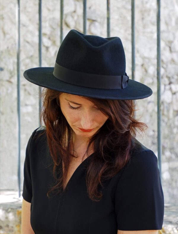 Femme brune devant grille avec chapeau noir en feutre